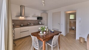 A modern kitchen with a dining area, including a wooden table and white chairs. - Appartamento Lucia by Theater Home - with big balcony and a panoramic view (Tignale)