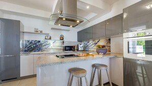 A modern kitchen with a marble backsplash, stainless steel appliances, and a central island with stools. - Private Seaside Villa Sleeps 10 With Infinity Pool (Zupa dubrovacka)