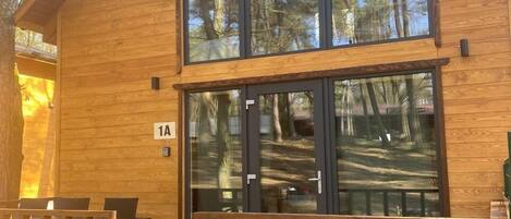 A wooden cabin with large glass windows, a wooden deck, and a staircase leading to the entrance.