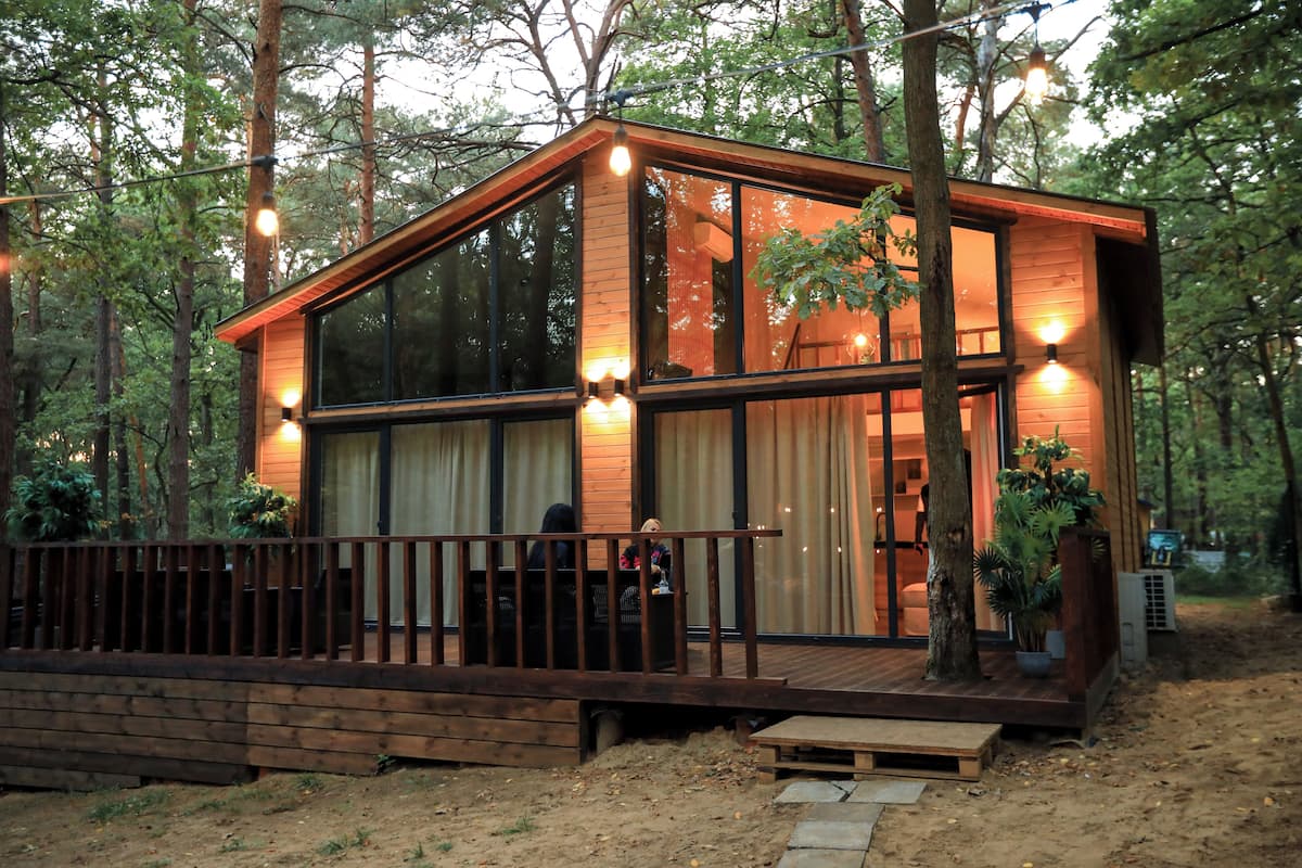 A modern wooden cabin with large windows, a deck, and a wooden fence.