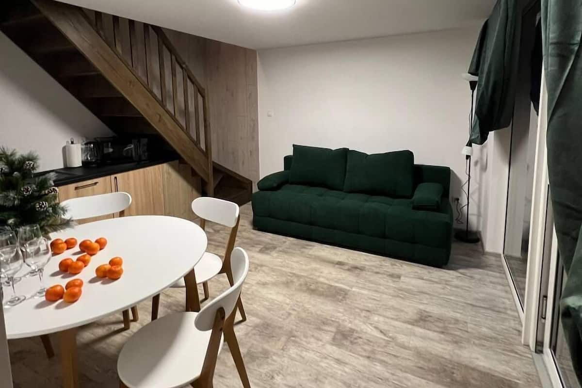 A modern kitchen with wooden cabinets, a dining table with white chairs, and a green sofa in the living area.