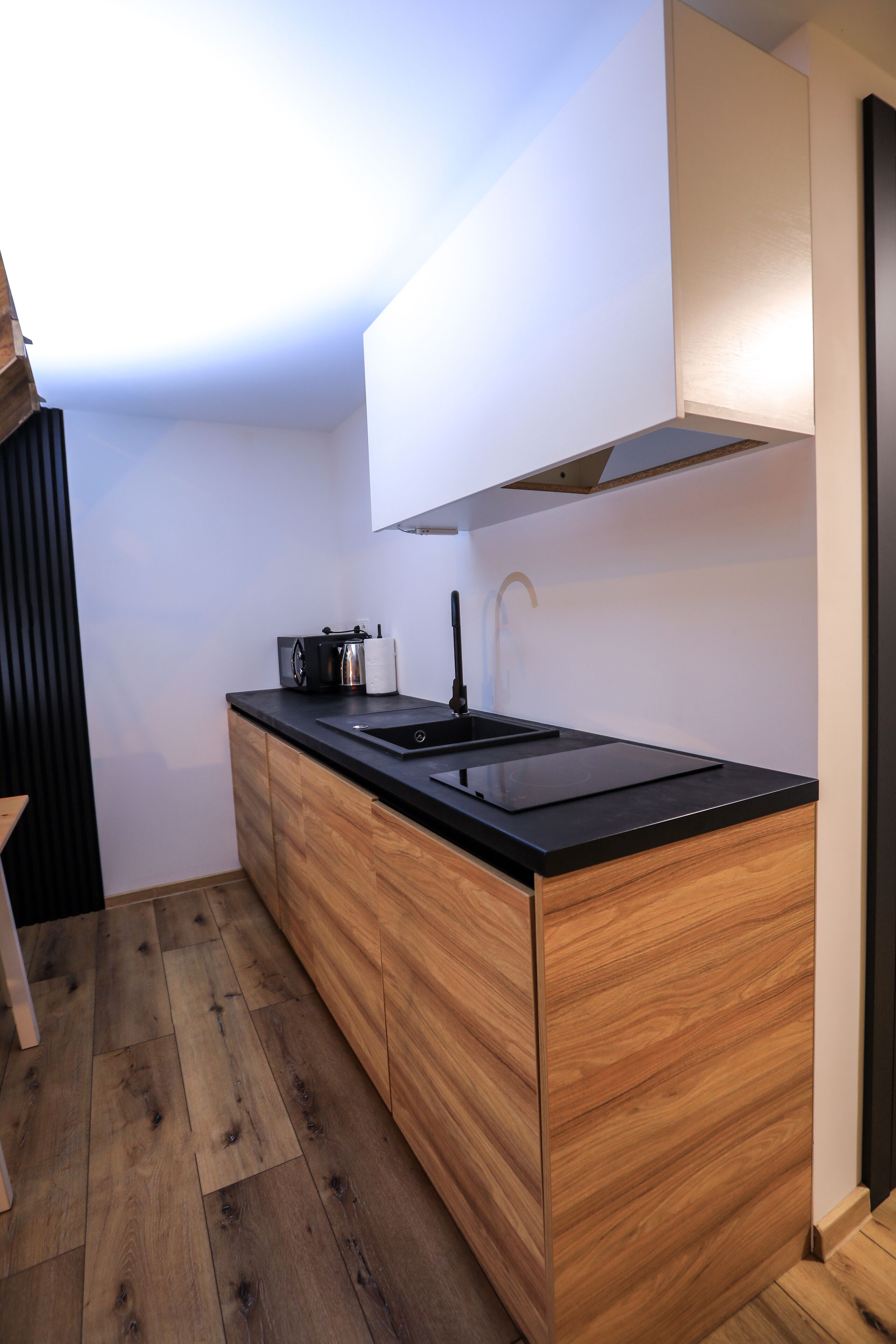 A modern kitchen with a black countertop, wooden cabinets, and a stainless steel sink.