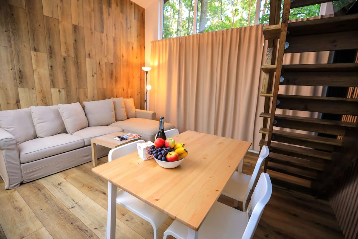 A wooden-floored living area with a sofa, a dining table with a fruit bowl, and a staircase.