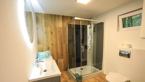 A modern bathroom with a wooden floor, a glass shower enclosure, a white sink, and a toilet. - Bizon Village (Piaseczno)