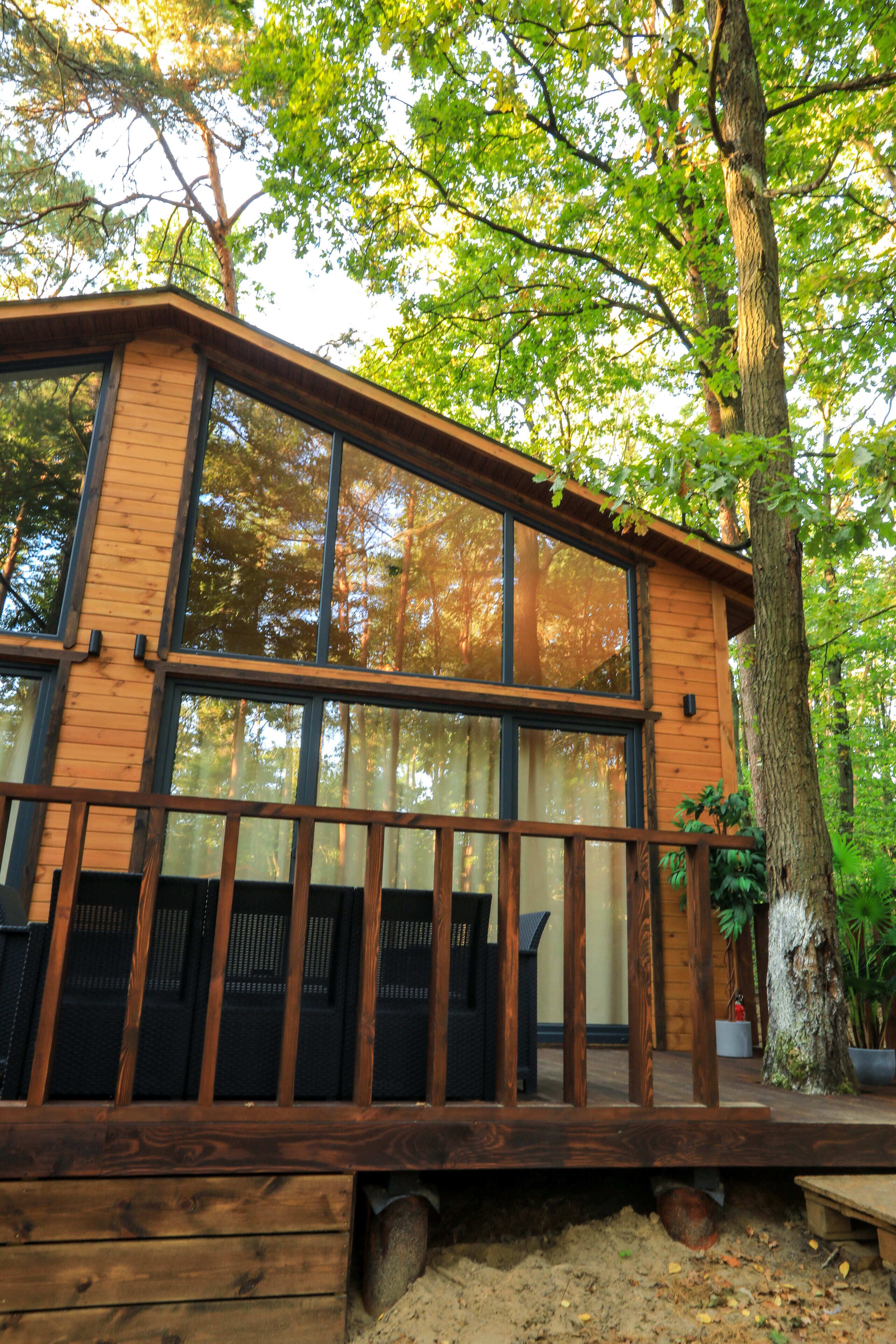 A wooden cabin with large windows, a deck, and a tree nearby.