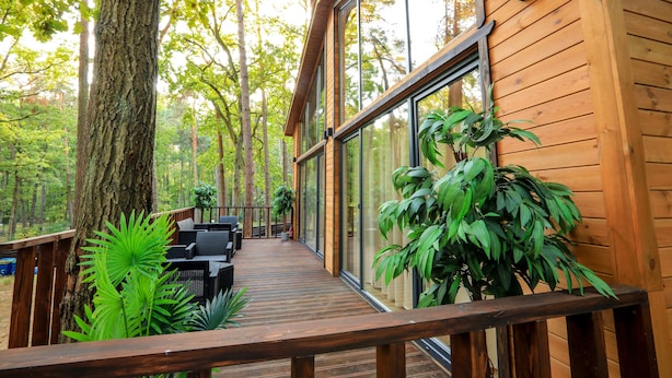 A wooden deck with outdoor furniture, surrounded by large trees and a glass wall. - Bizon Village (Piaseczno)