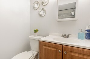 Un baño con lavamanos blanco, armarios de madera, un espejo y decoración en la pared.