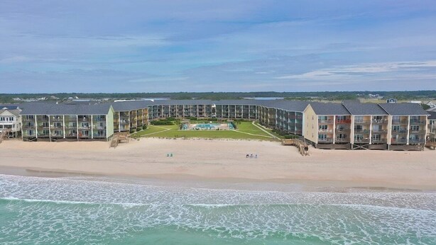 Un hotel frente a la playa con varias construcciones, una piscina y una playa de arena.