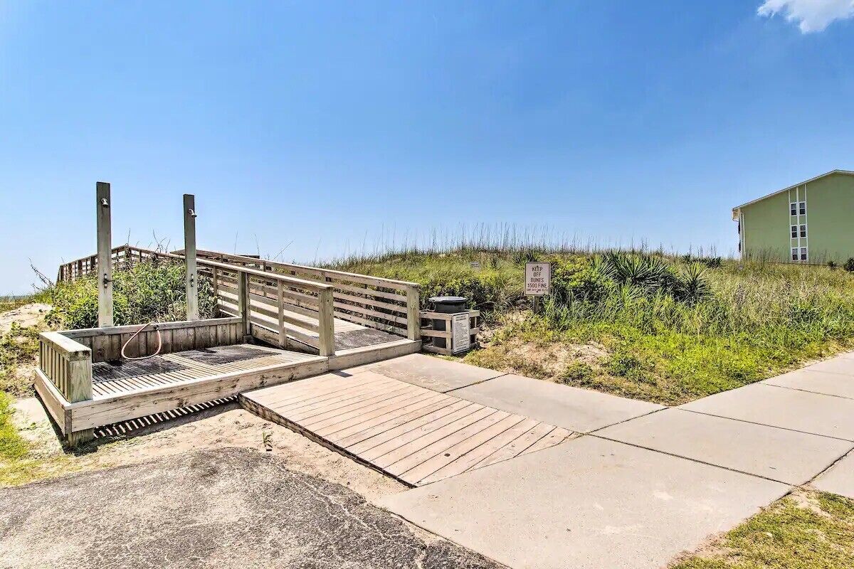 A wooden boardwalk leading to a beach area with a building in the background.