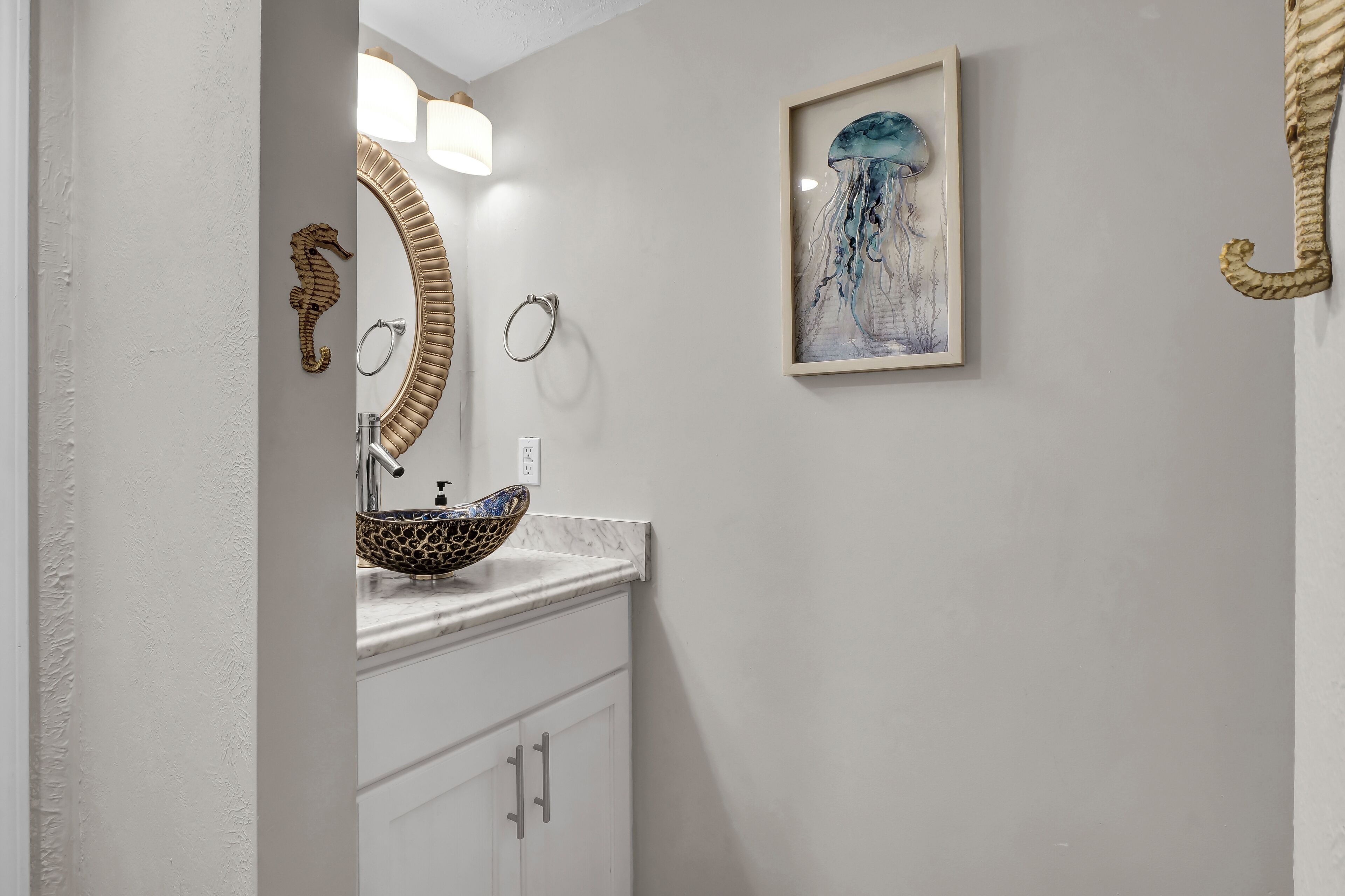 A bathroom with a white vanity, a seahorse decoration, a framed seahorse painting, and a unique seahorse-shaped mirror.