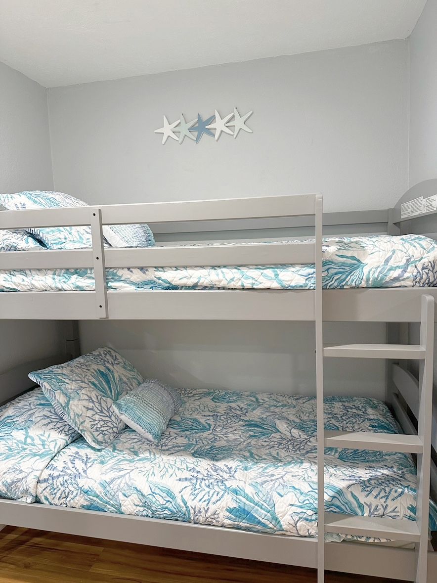A bunk bed with a white frame and patterned bedding, a wall-mounted star decoration, and a wooden floor.