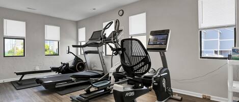 A gym with treadmills, an elliptical, and a rowing machine, featuring large windows and a clean, modern design.