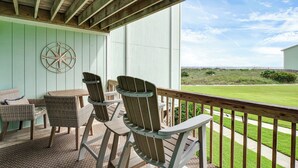 Un área de estar al aire libre techada con sillas Adirondack y una mesa, con vista a un paisaje con césped.