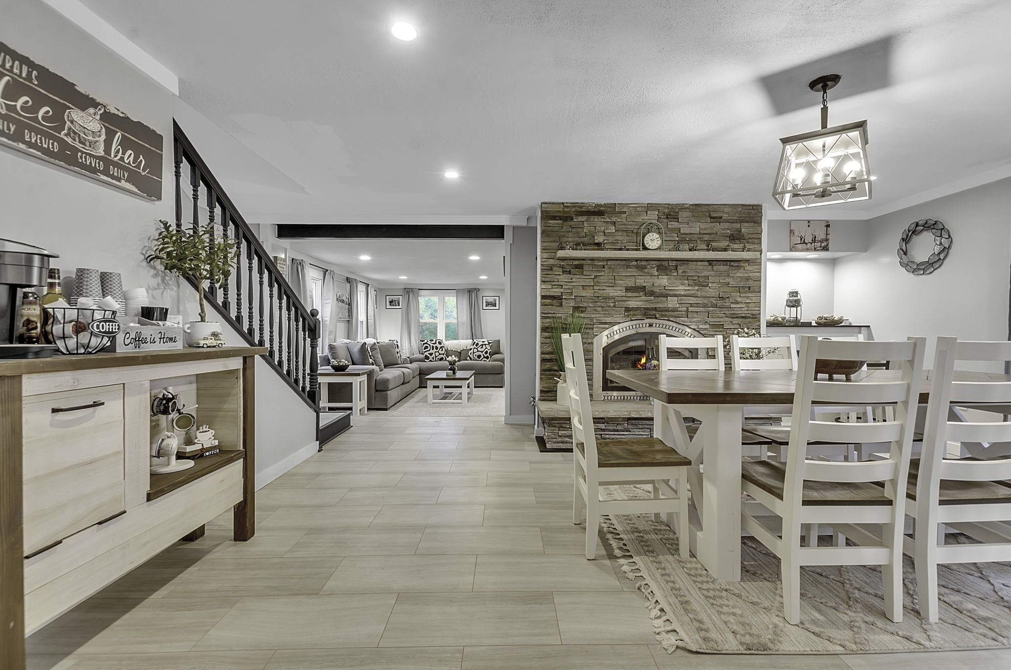 A modern living room with a fireplace, a dining area with white chairs, and a kitchen area with a coffee station.