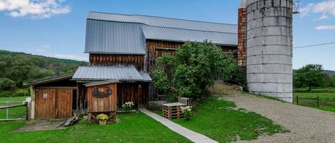 A rustic barn with a silo, wooden exterior, and a gravel driveway.