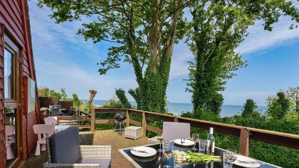 An outdoor dining area with a view of the sea, furnished with wicker chairs and a table set for two. - The Lookout, Sunny Beach Retreat, Sleeps 5 Guests (Deal)