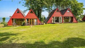 A row of red triangular cabins with large windows, a grassy lawn, and trees in the background. - The Lookout, Sunny Beach Retreat, Sleeps 5 Guests (Deal)