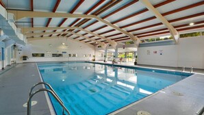 An indoor swimming pool with a clear ceiling and walls, a lifeguard station, and a poolside area with a chair and potted plants. - The Lookout, Sunny Beach Retreat, Sleeps 5 Guests (Deal)