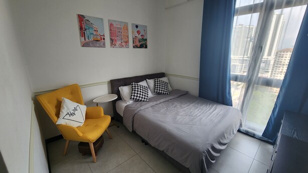 Une chambre d’hôtel moderne avec un lit, un fauteuil jaune, une petite table ronde et trois œuvres d’art accrochées au mur.