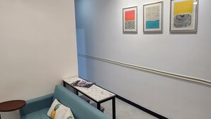 Une pièce moderne avec un canapé bleu, une petite table et un ventilateur de plafond. Trois œuvres d’art encadrées ornent le mur.