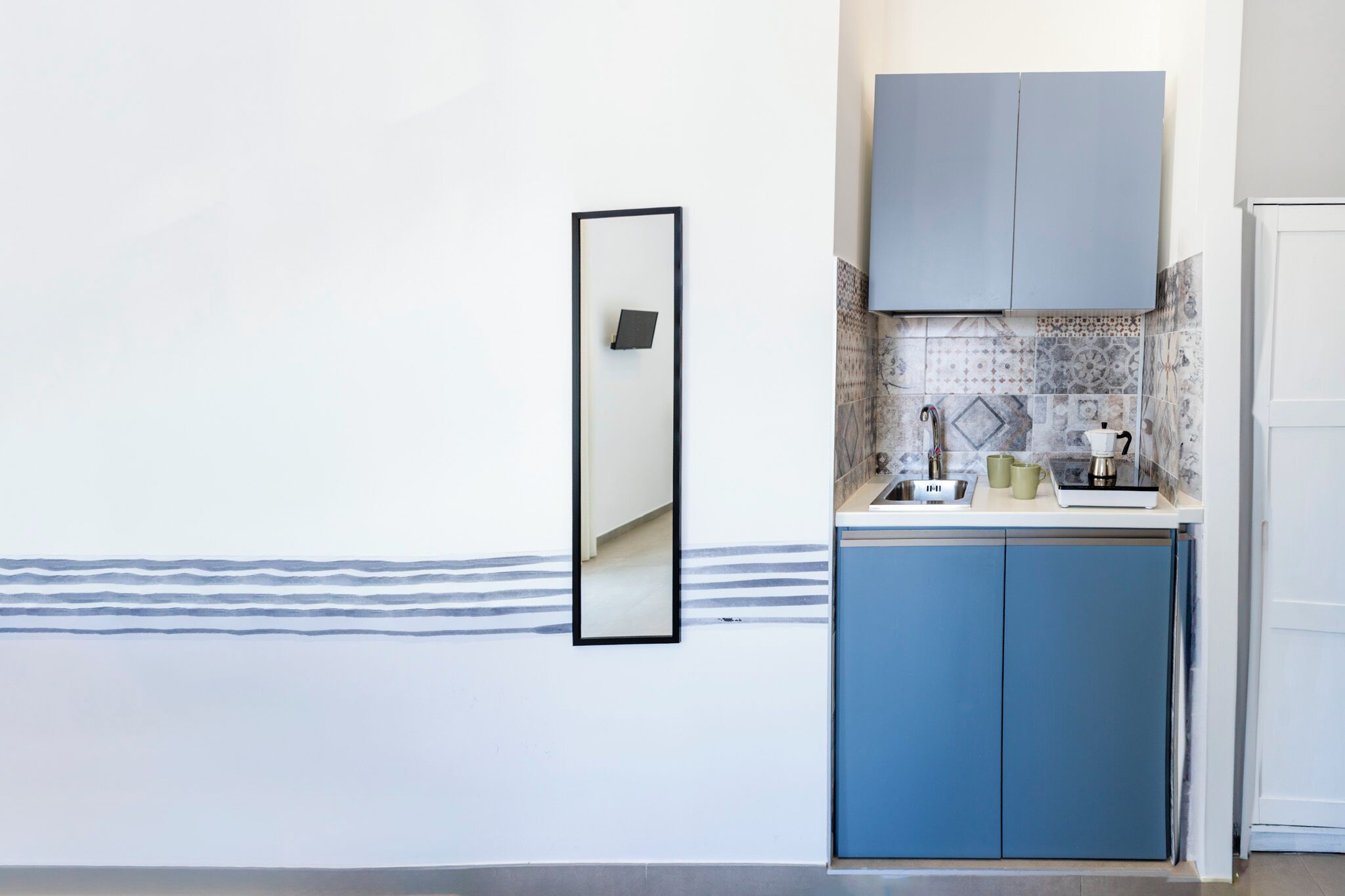 Une cuisine compacte avec des meubles bleus, un plan de travail blanc et un pare-feu en carreaux.