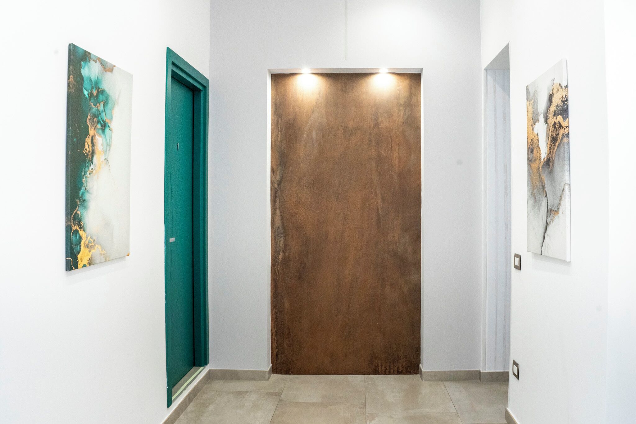 Un pasillo con una puerta verde azulada, una puerta marrón y dos cuadros abstractos en las paredes.