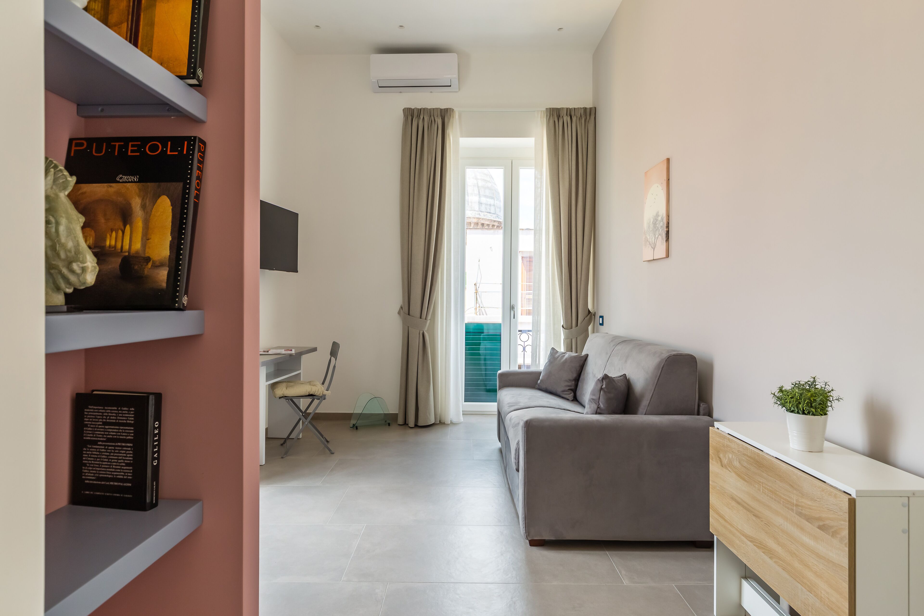 Una sala de estar moderna con un sofá gris, un escritorio pequeño y una estantería.