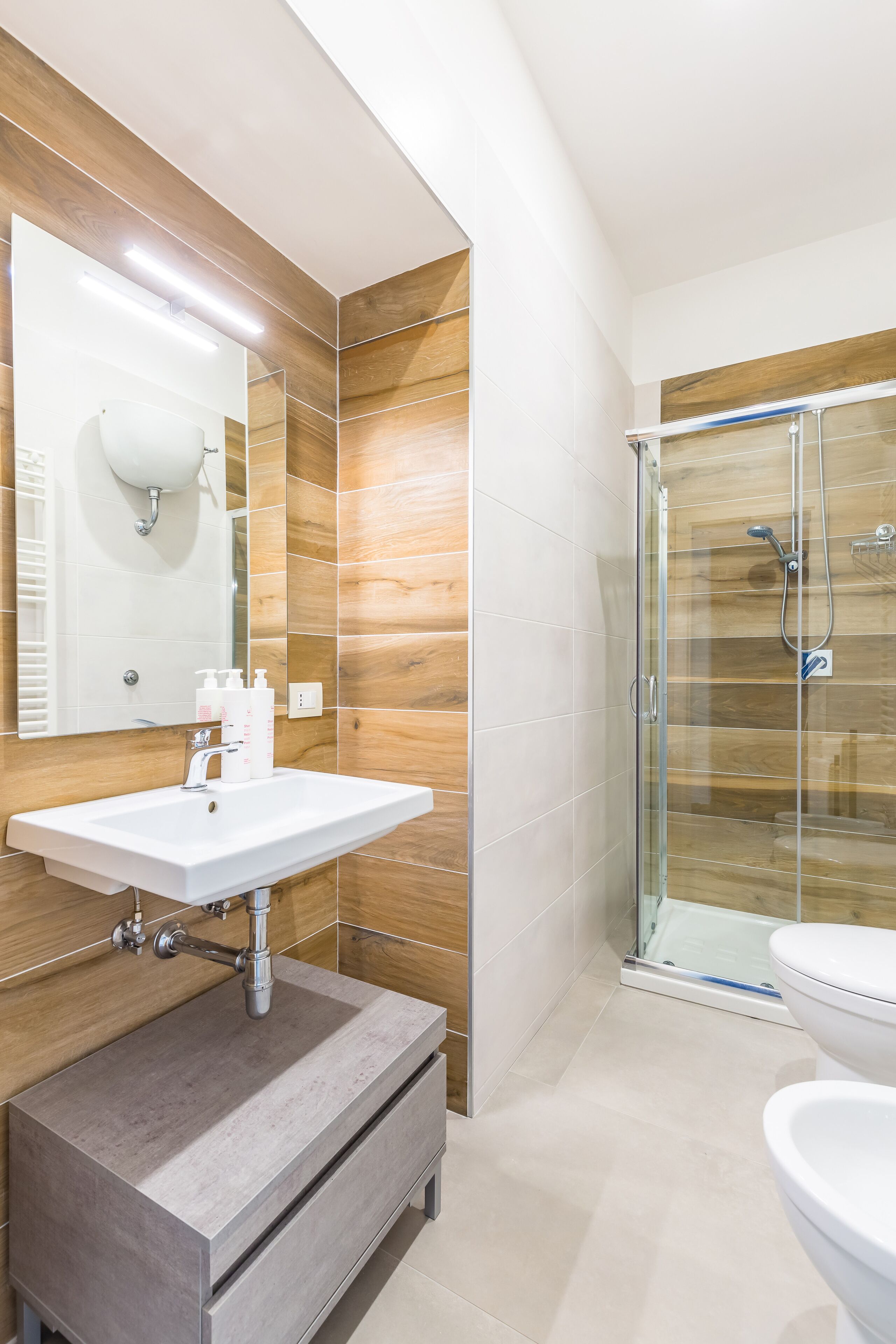 A modern bathroom with a large mirror, a sink, a shower enclosure, and a toilet.