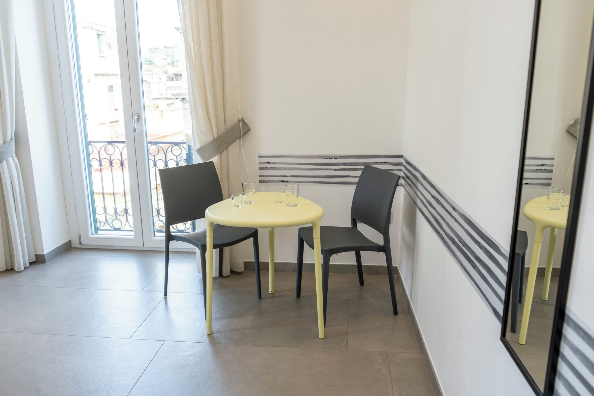 Ein kleiner Raum mit einem gelben Tisch und zwei Stühlen, einem großen Spiegel und einer Glastür, die auf einen Balkon führt.