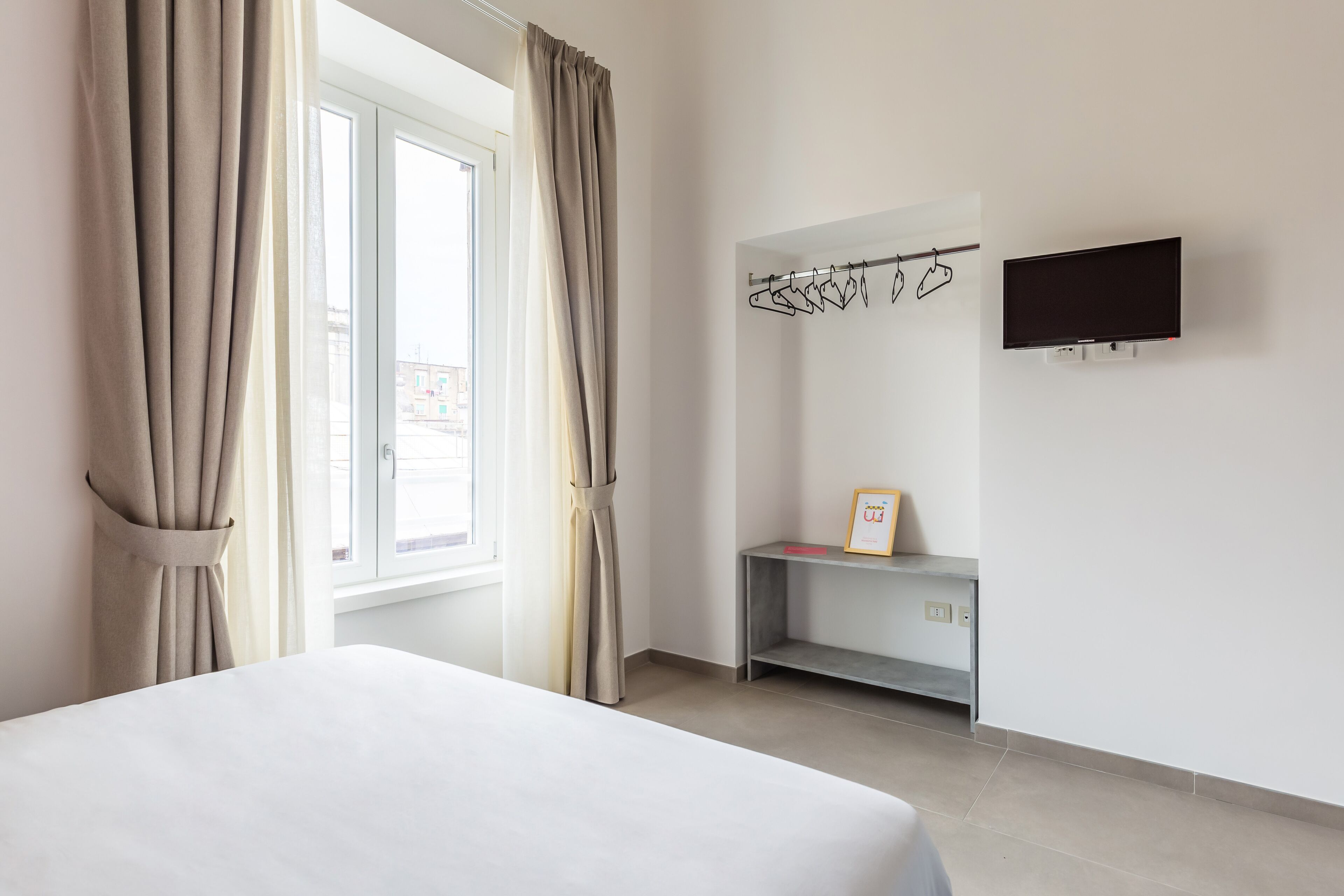 Een hotelkamer met een bed, een bureau, een televisie en een raam met gordijnen.