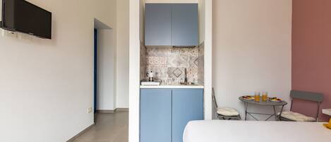 Habitación de hotel con cama, kitchenette pequeña, televisor montado en la pared y zona de comedor con mesa y sillas.