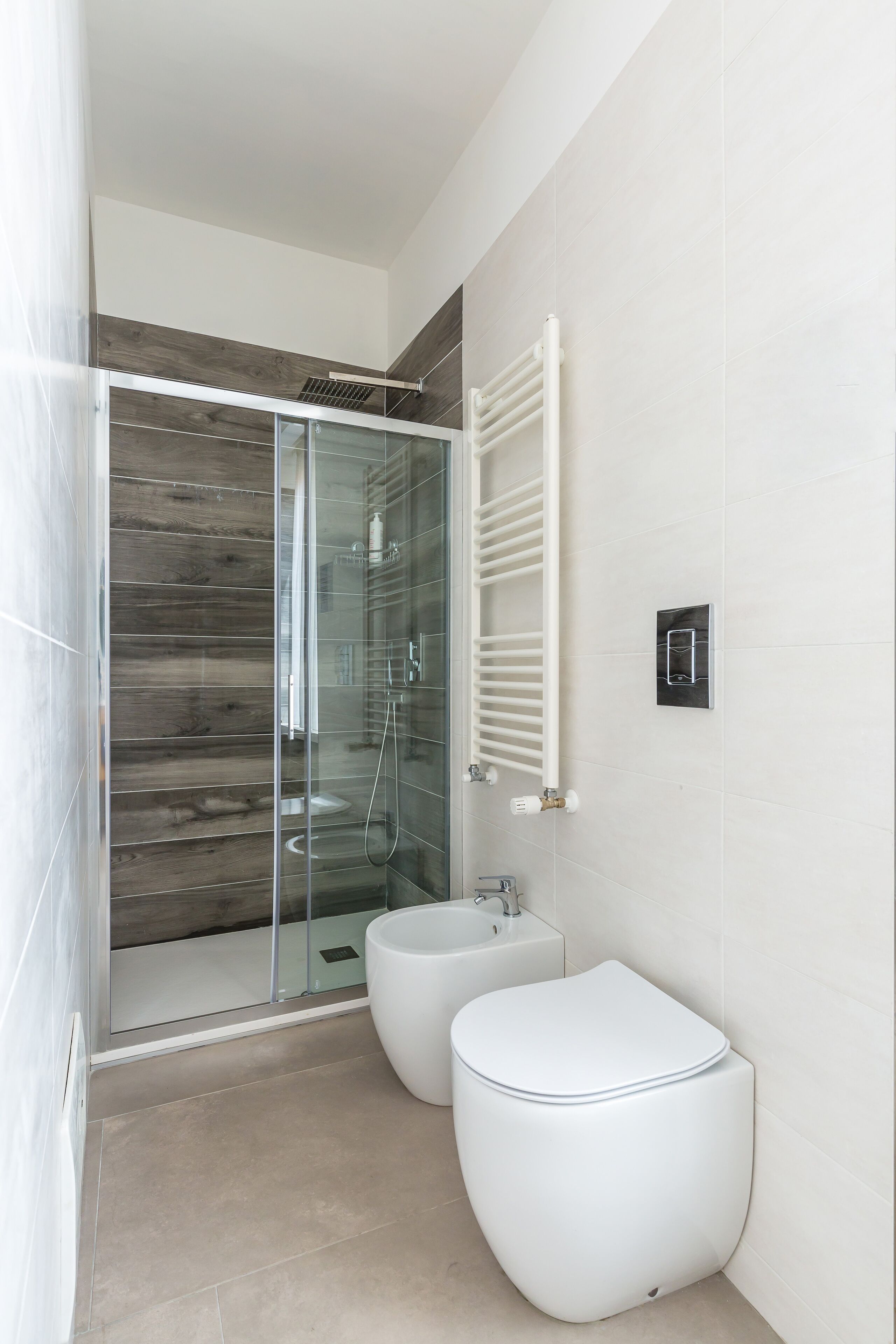 A modern bathroom with a glass-enclosed shower, a white toilet, and a bidet.