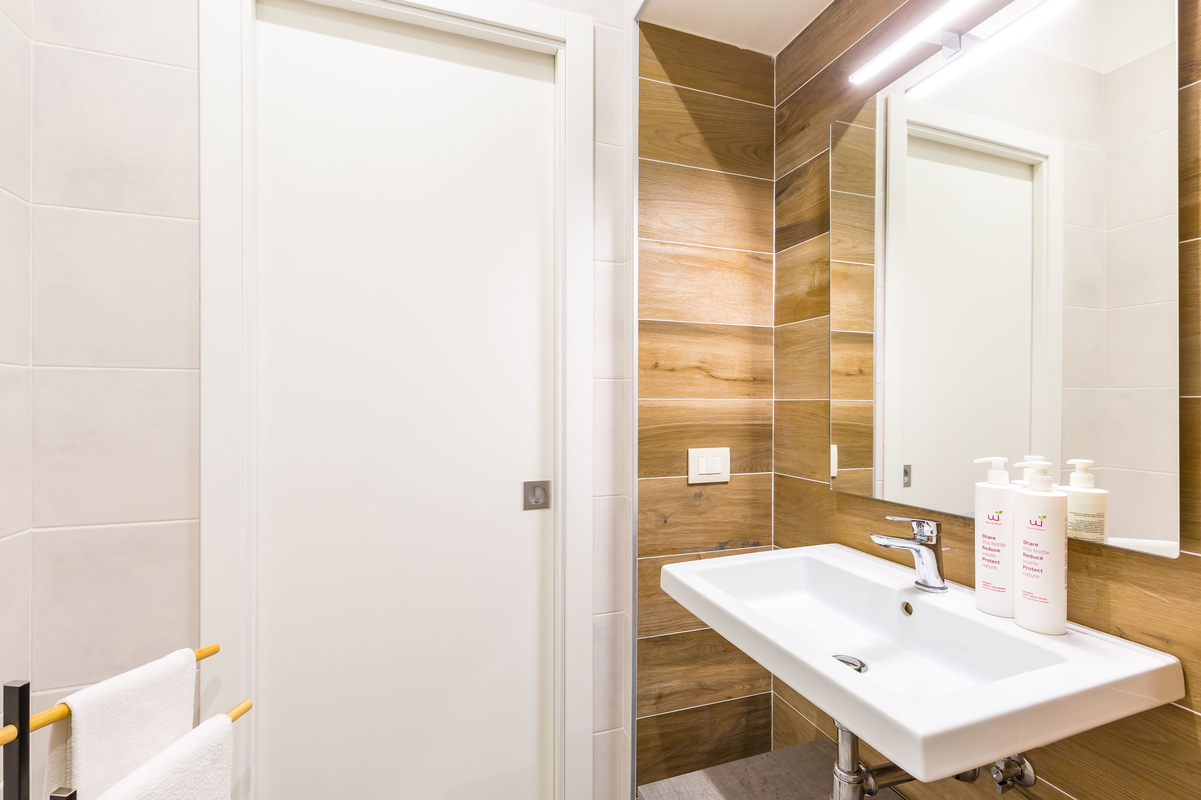 A modern bathroom with a white sink, wooden wall tiles, and a mirror above it.