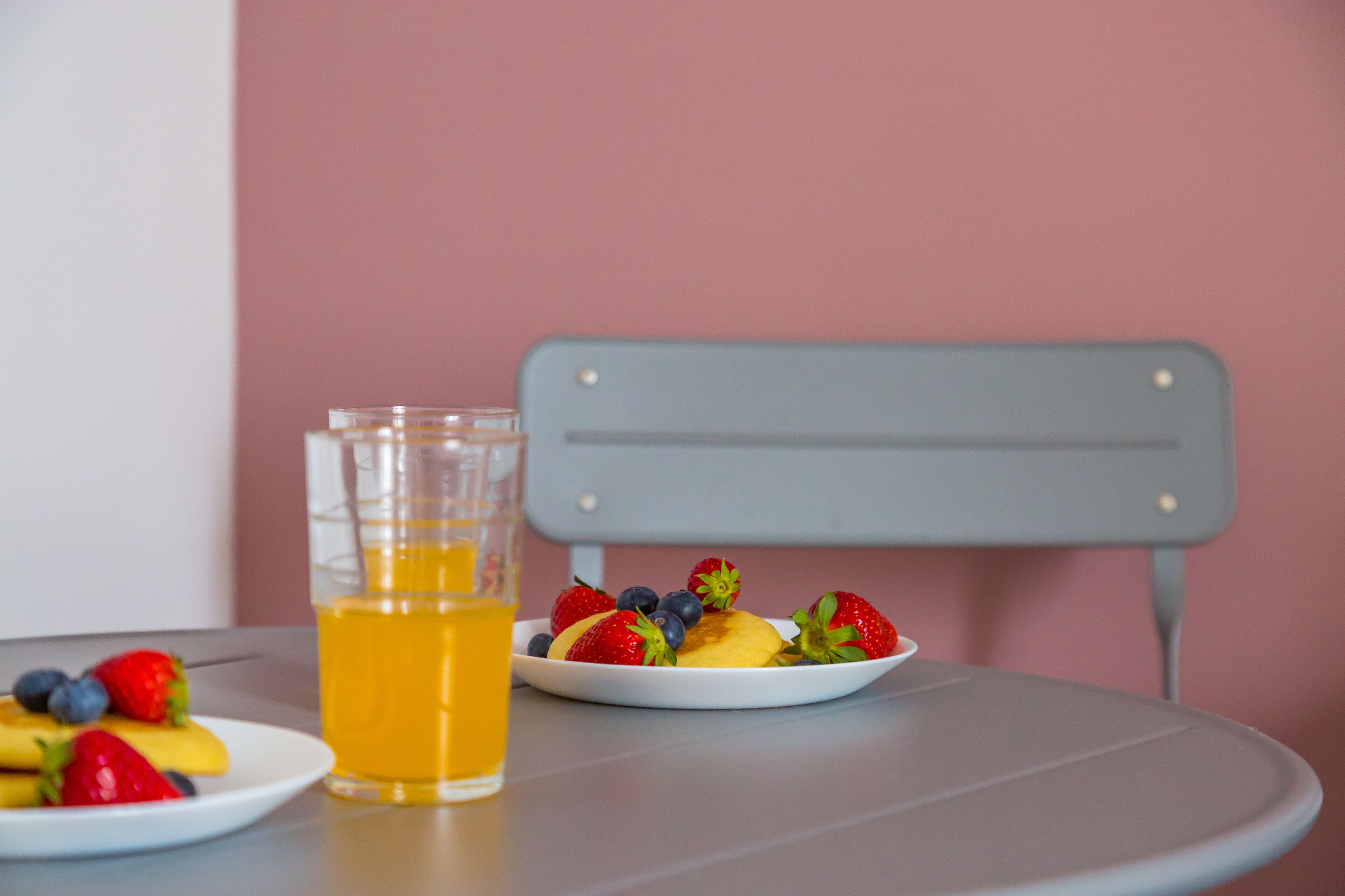 A table with a glass of orange juice, a plate with strawberries and blueberries, and another plate with bananas and strawberries.
