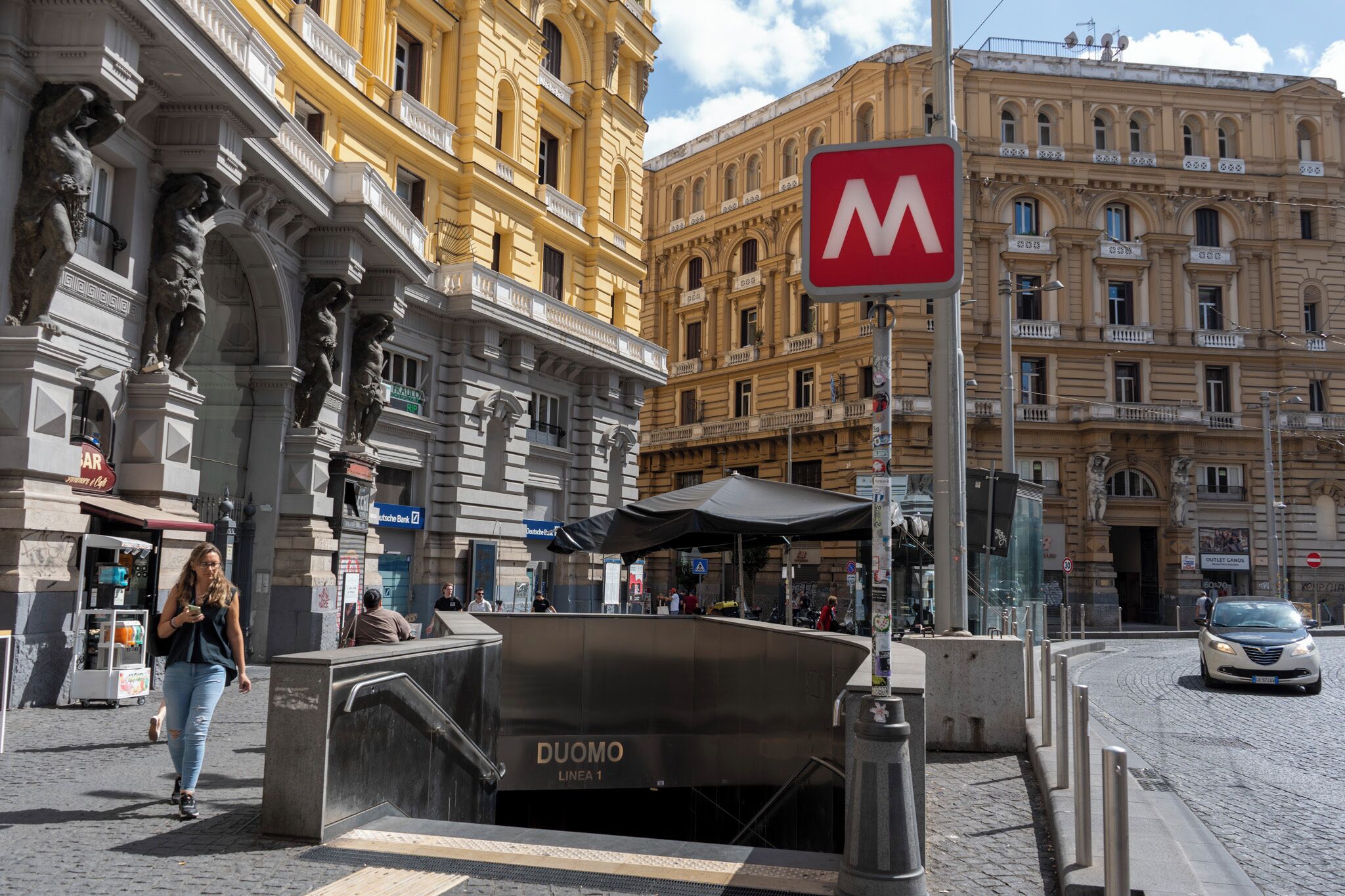 A street scene with a prominent 'M' sign, historic buildings, and a Duomo Linea 1 entrance.
