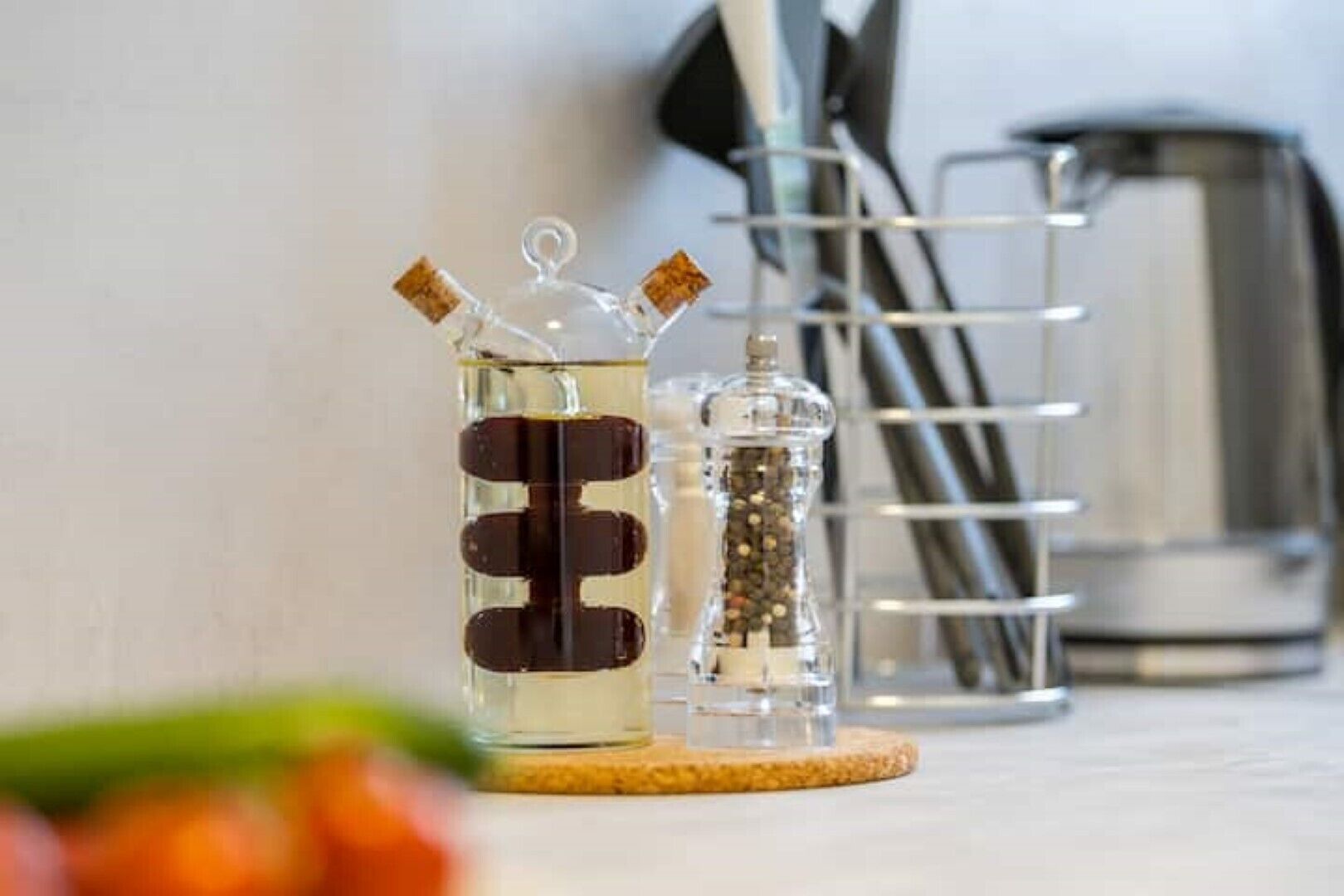 A kitchen counter with a glass container holding a dark liquid, a glass container with a cork stopper, and a metal utensil holder.