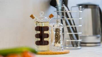A kitchen counter with a glass container holding a dark liquid, a glass container with a cork stopper, and a metal utensil holder.