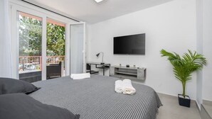 Ein modernes Schlafzimmer mit einem großen Bett, einem Fernseher, einem Schreibtisch und einem Balkon mit Geländer.