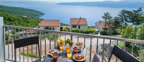 A balcony with a table set for breakfast overlooking a coastal view.