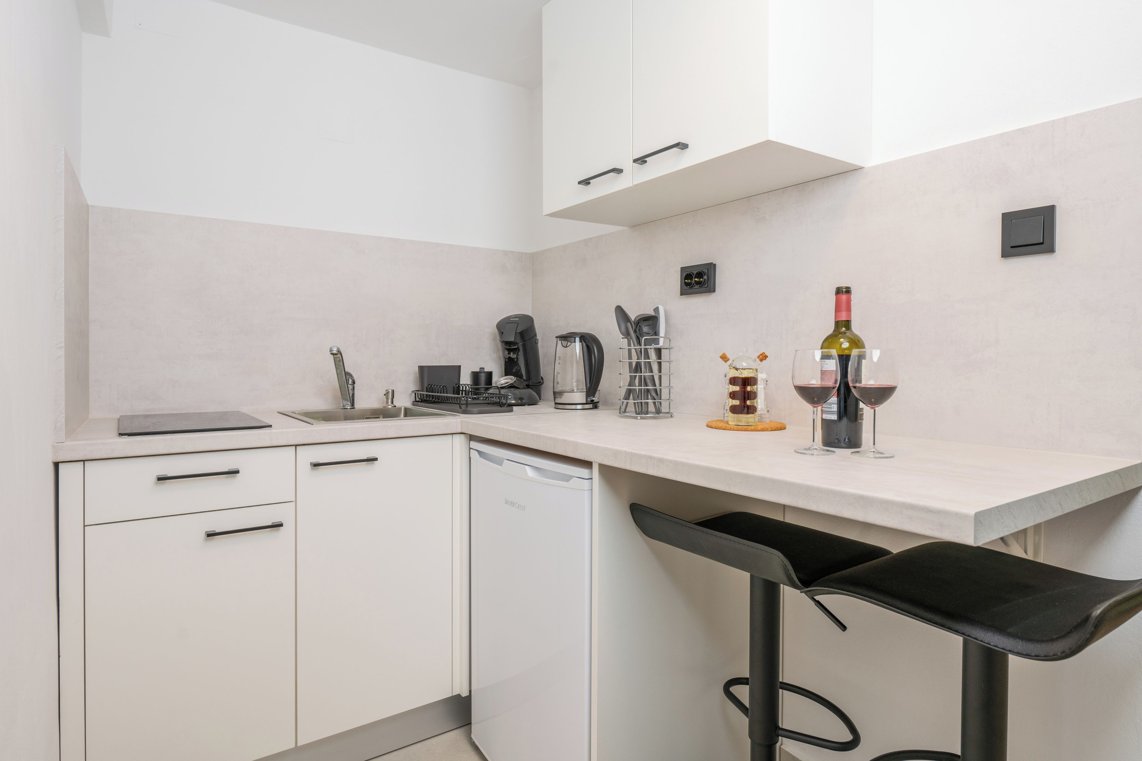 A modern kitchen with white cabinets, a built-in dishwasher, a coffee machine, and a wine bottle.