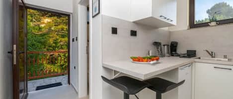 A modern kitchen with white cabinets, a countertop, and a window overlooking greenery.