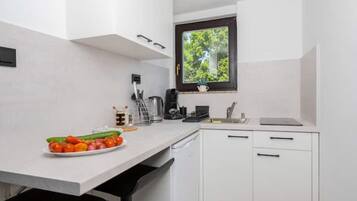 Una cocina compacta con armarios blancos, una ventana con vistas a zonas verdes, un lavamanos y una encimera con un plato de verduras.