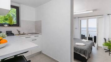 A compact hotel room with a kitchenette, a balcony with a view, and a bed with a striped bedspread.