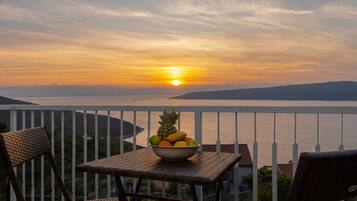 A balcony with wicker furniture, a bowl of fruit, and a sunset view over water.