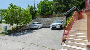 Un área de estacionamiento con dos coches, un muro de piedra y una escalera que conduce a un edificio.