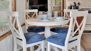 Una mesa redonda blanca con cuatro sillas, cada una con un cojín azul. La mesa está servida con un plato blanco, un tazón azul y un vaso.