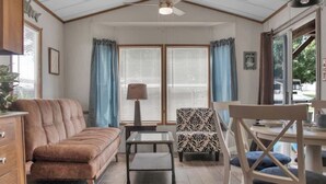Una habitación acogedora con un sofá marrón, un sillón estampado, una mesita y un ventilador de techo.