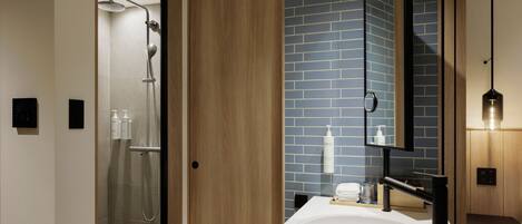 A modern bathroom with a glass-enclosed shower, a wooden door, a blue-tiled wall, a white sink, and a mirror.