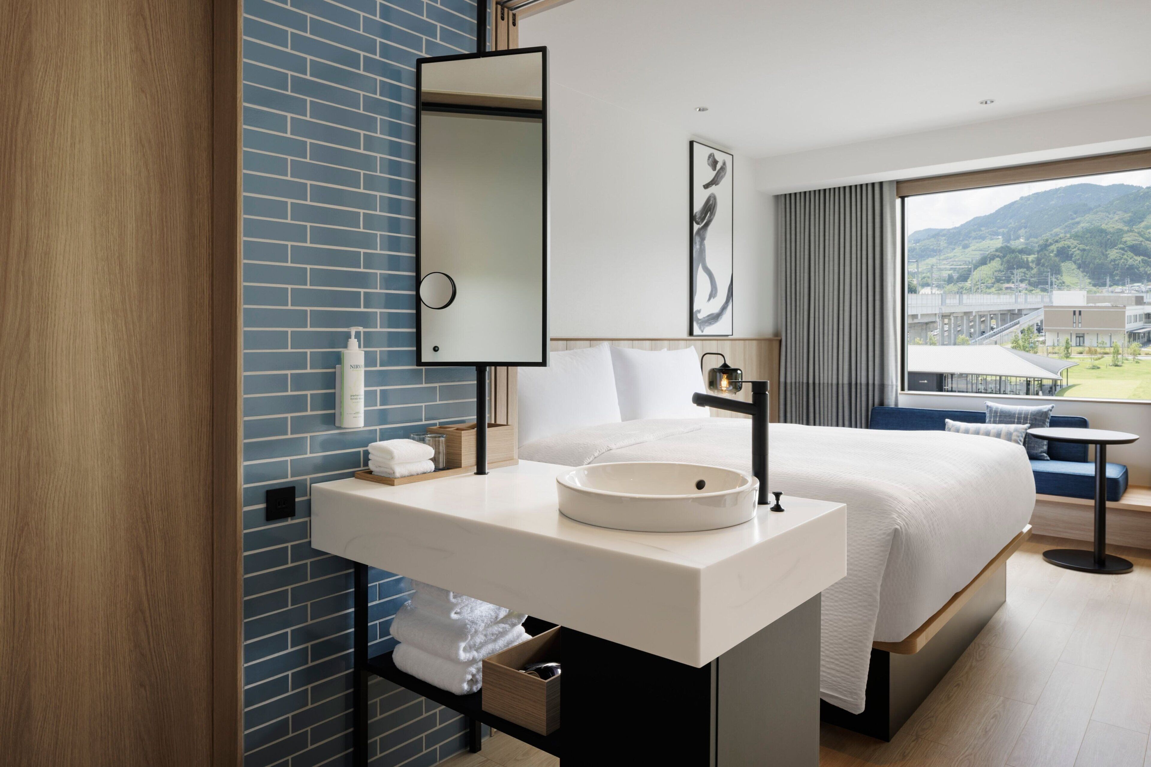Quarto de hotel moderno com uma cama grande, pia branca, espelho e vista para as montanhas pela janela.