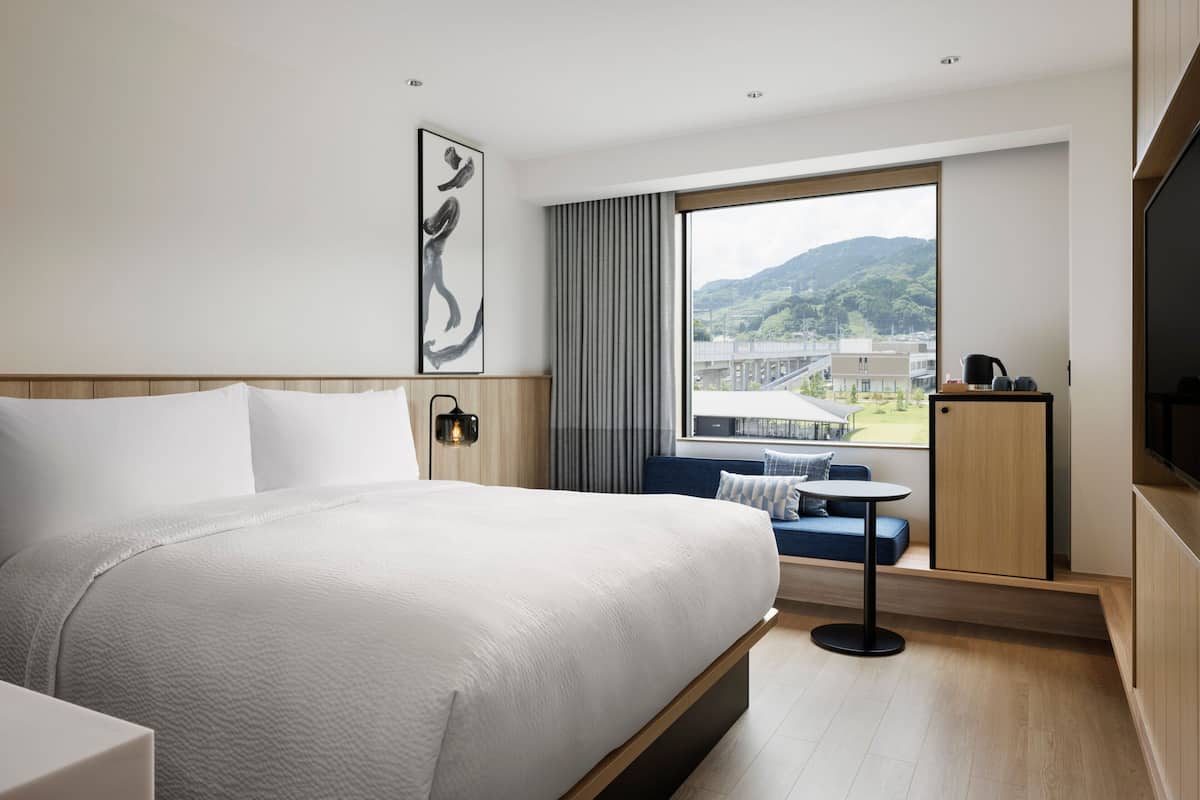 Ein modernes Hotelzimmer mit einem großen Bett, einer Sitzecke am Fenster und einem Fernseher.